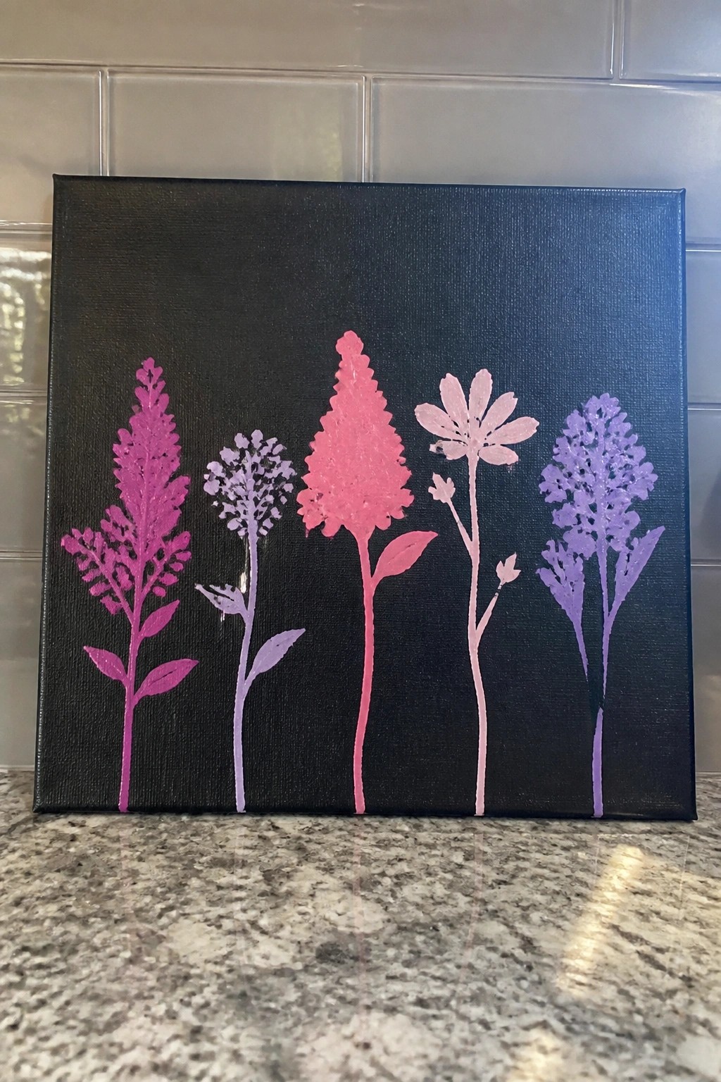 Black canvas with five pink and purple stylized flowers on granite counter.