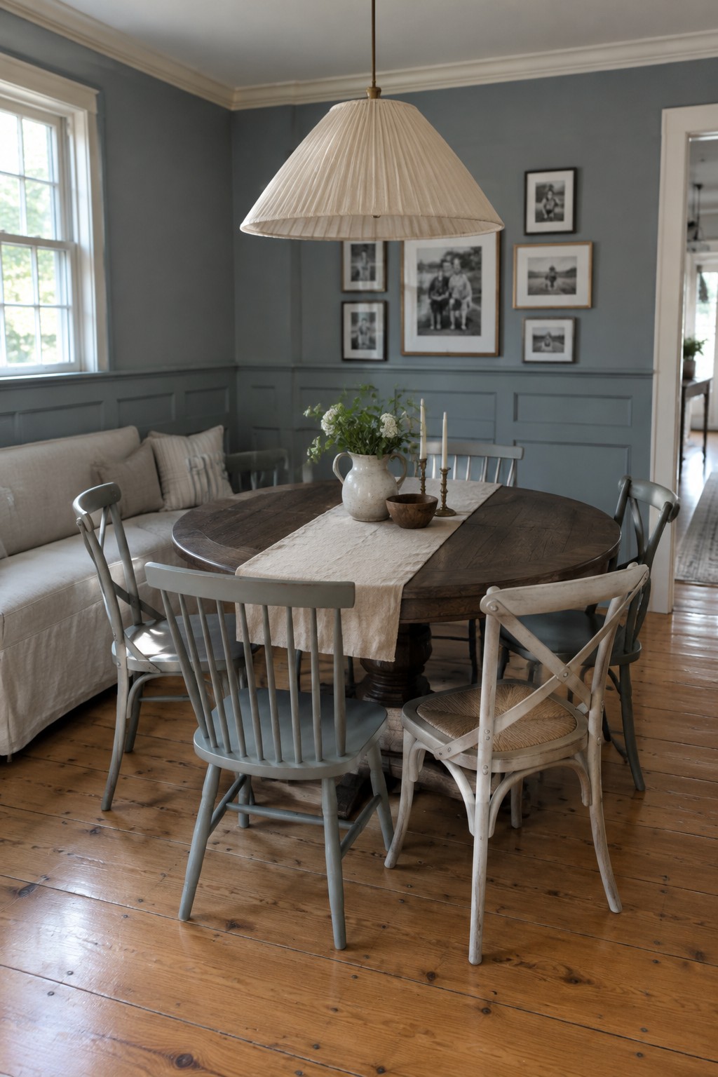 Round wood dining table with mixed chairs, floral runner, and blue walls.