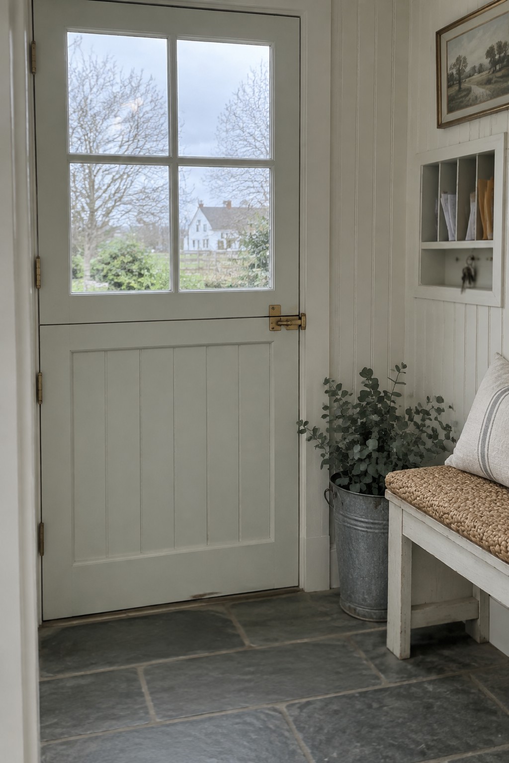 Sage green door with glass panes, white bench, potted plant on slate floor