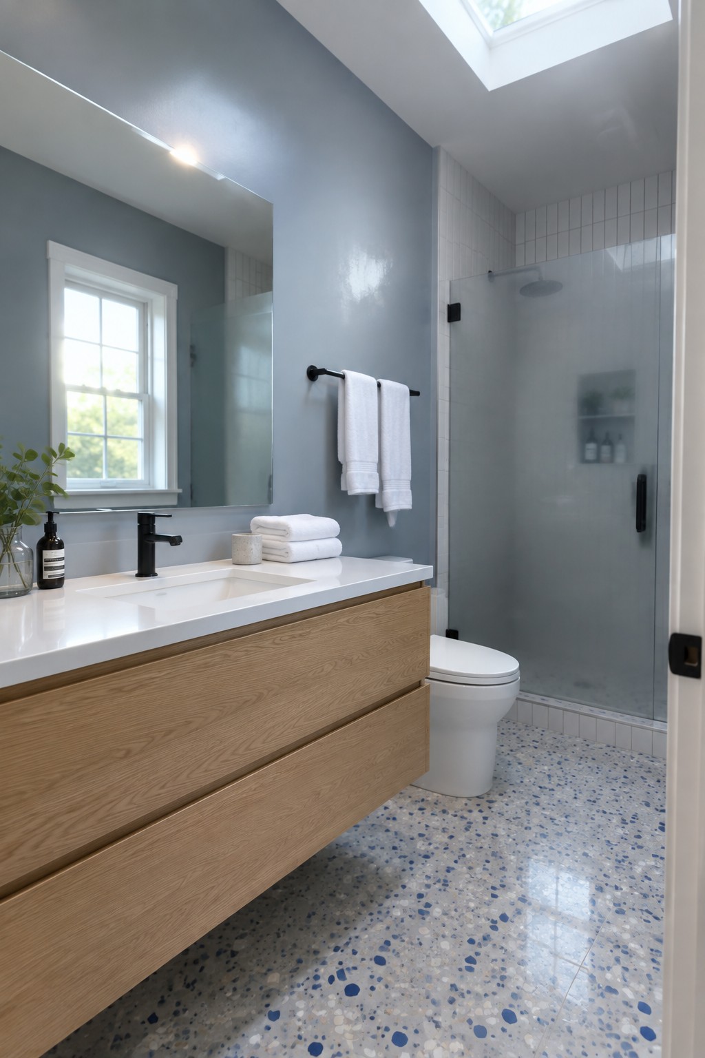 A bathroom with soft blue gray walls, white tile, and a light wood vanity.