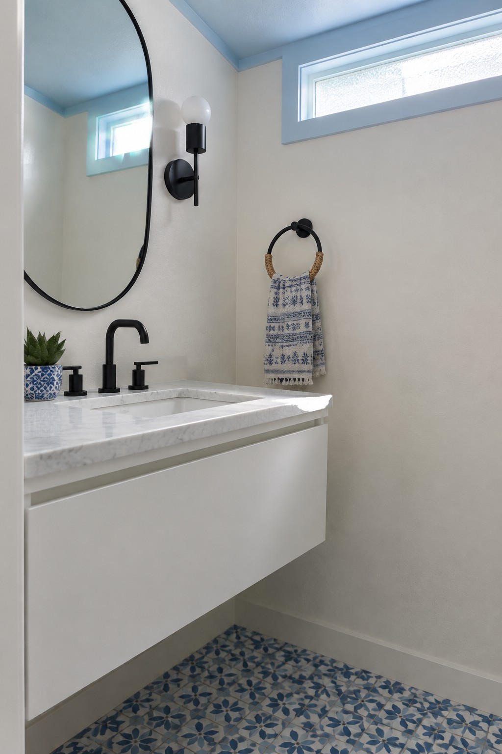 A small bathroom with warm white walls, a floating white marble vanity, and blue patterned tile on the floor.