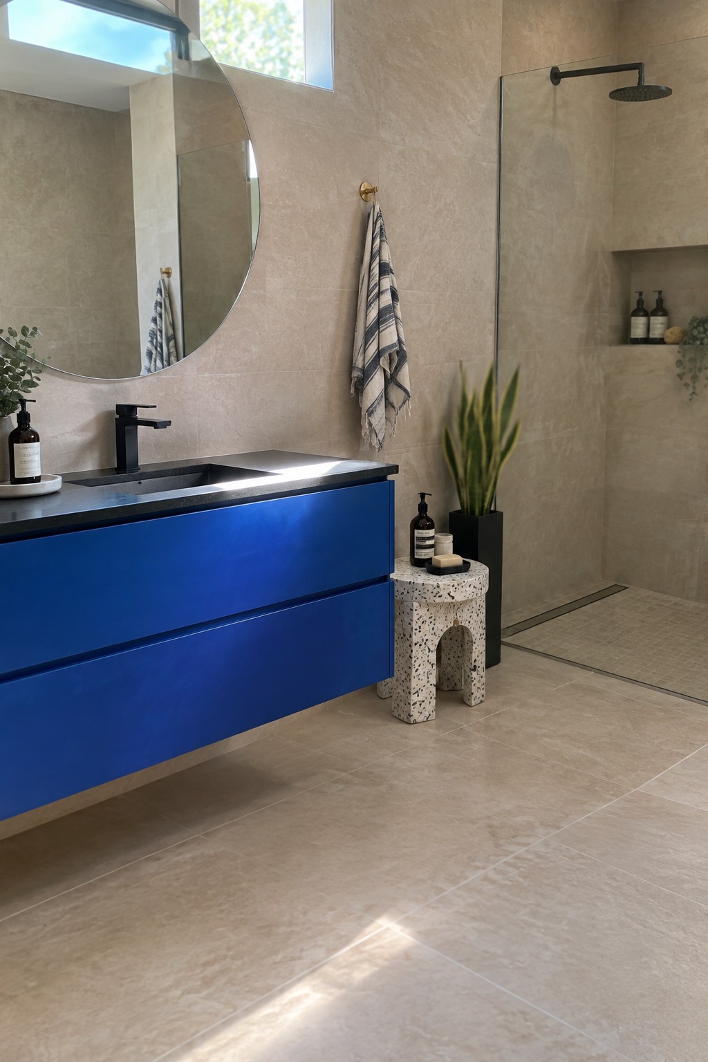 A vibrant blue floating vanity with a dark stone top in a neutral tiled bathroom.