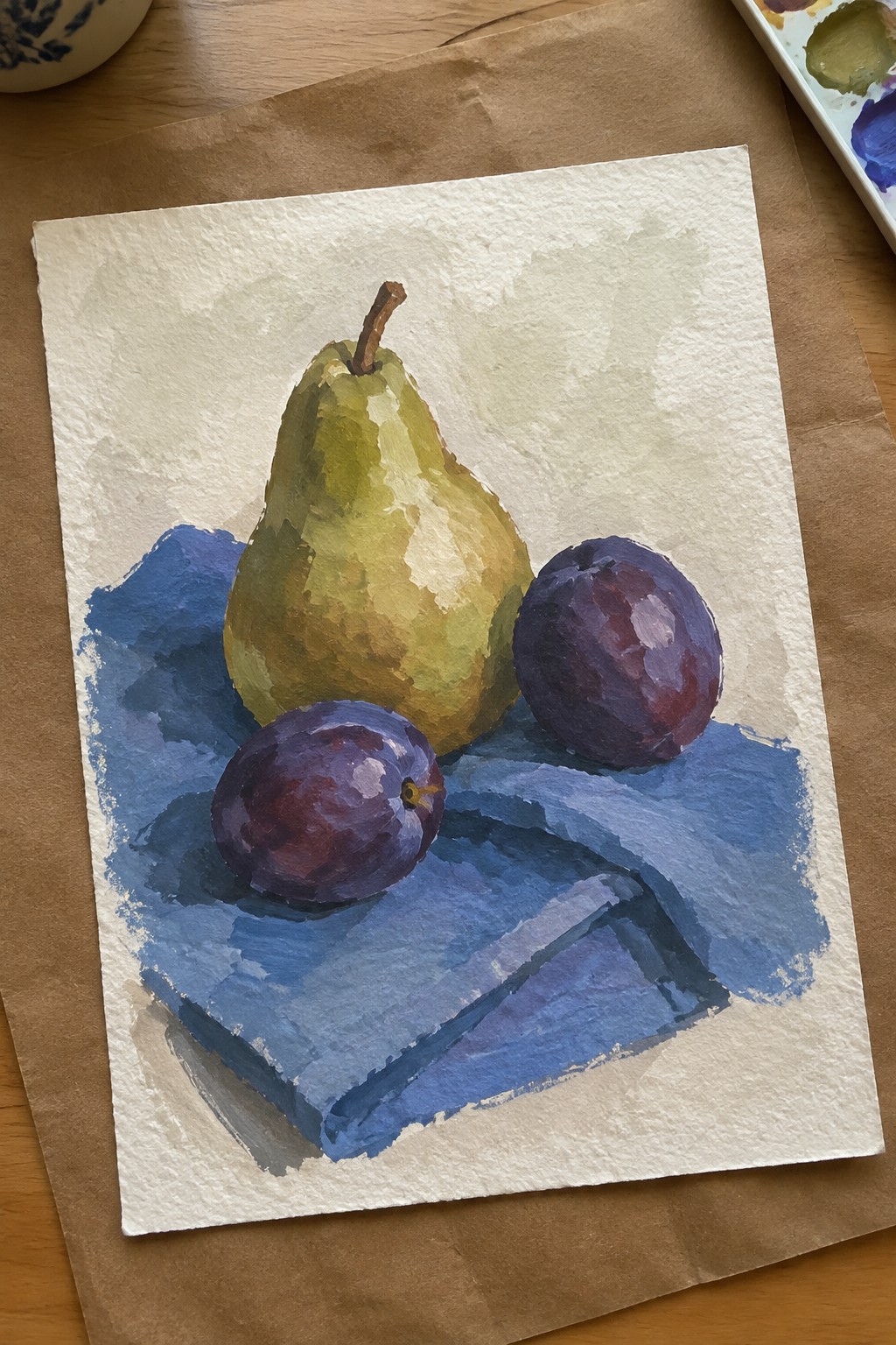 Watercolor still life of green pear and two purple plums on blue cloth.