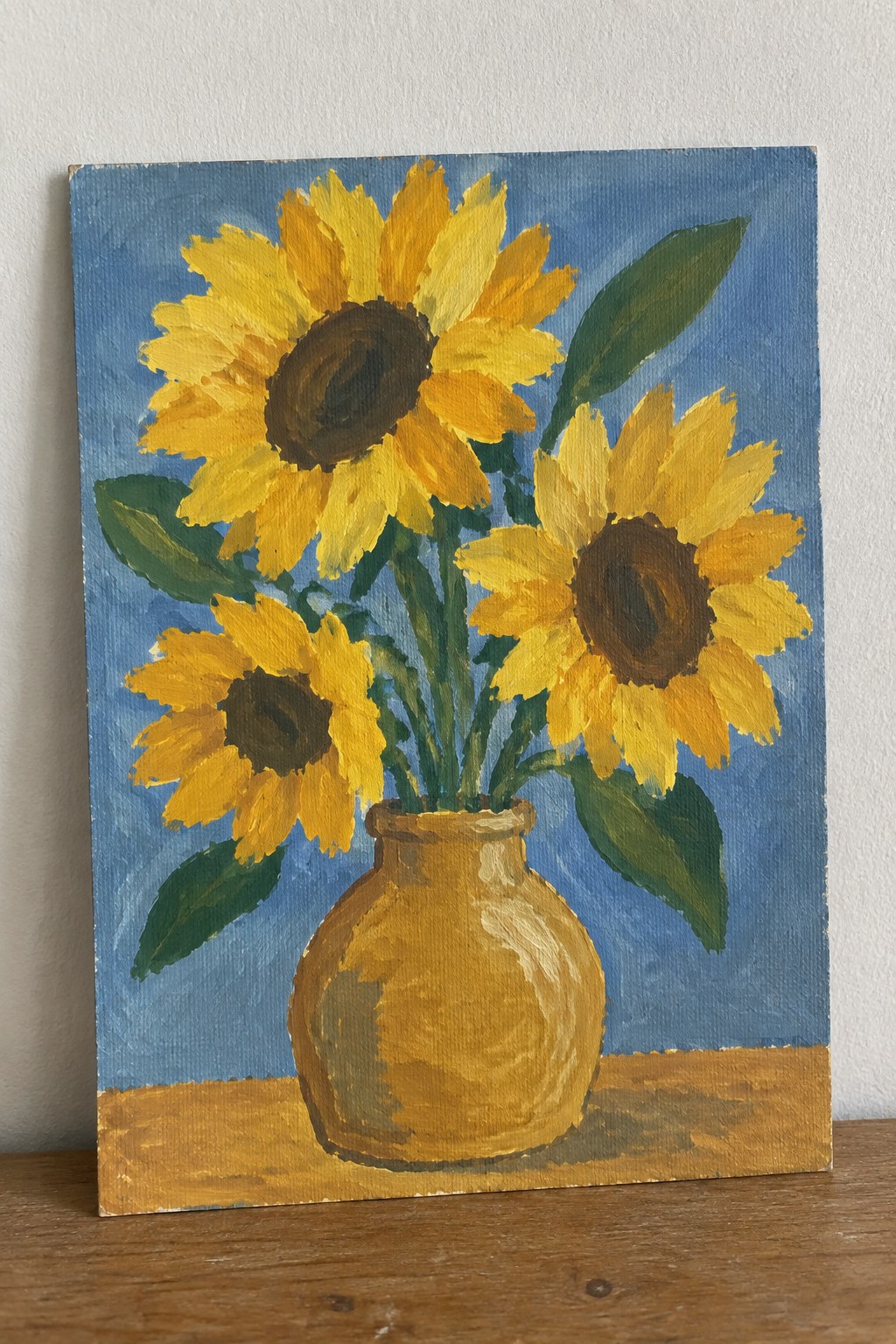 Three yellow sunflowers in a vase on a brown table with blue background.