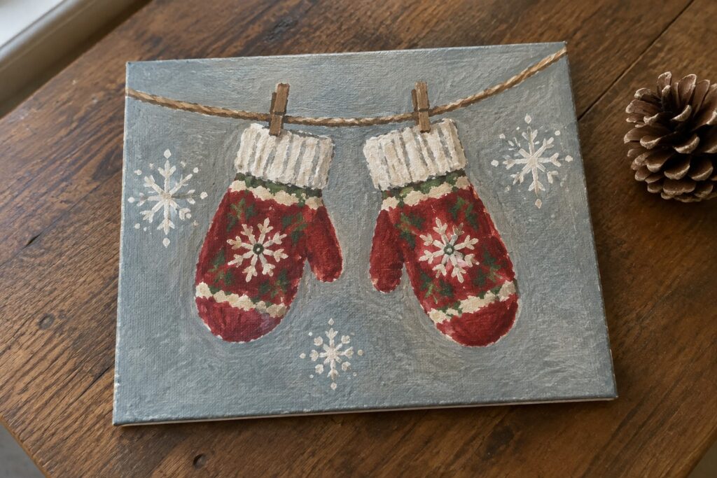 Two red snowflake mittens clipped to twine on gray canvas with white flakes