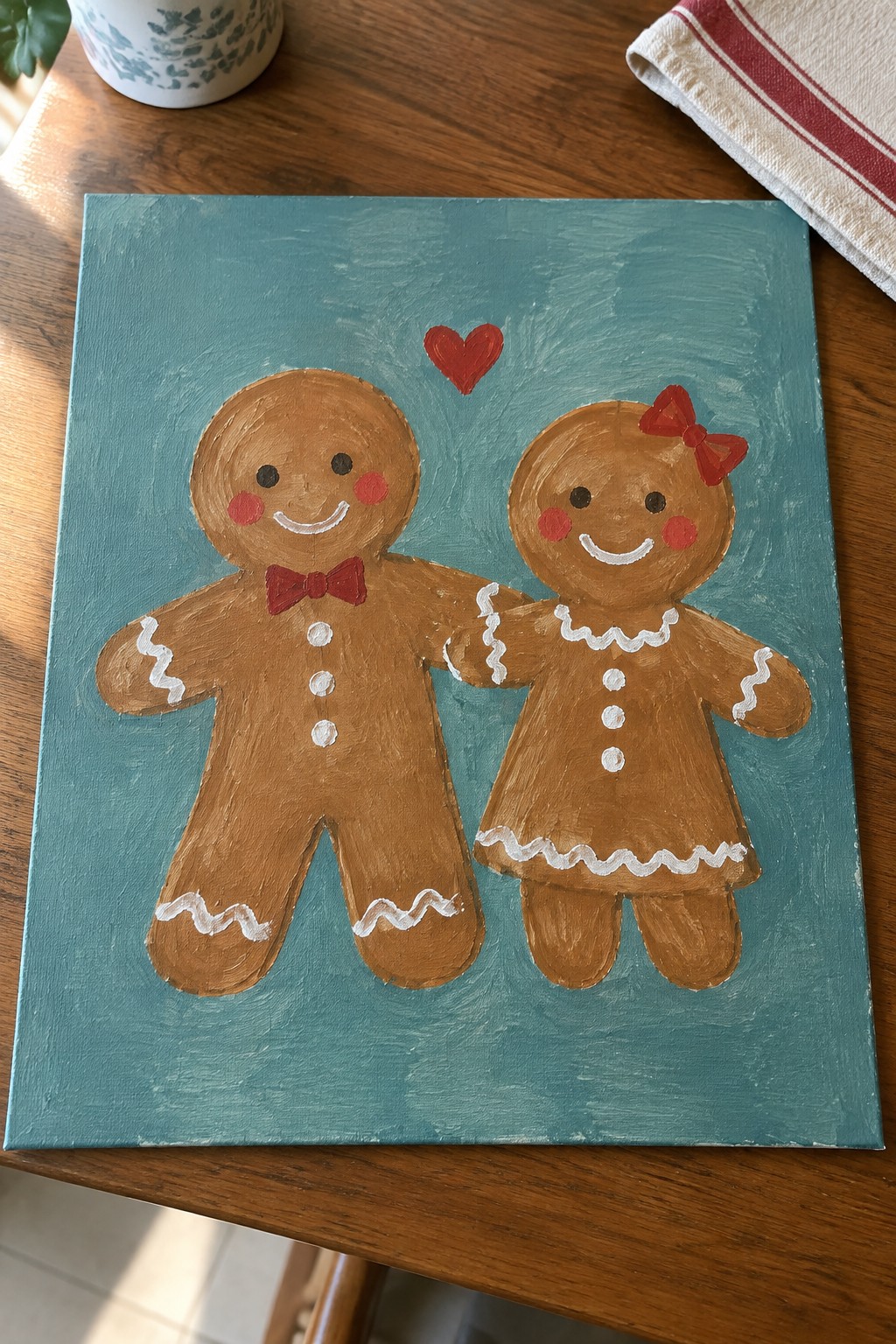 Gingerbread man with red bow tie and woman with bow on teal canvas with heart