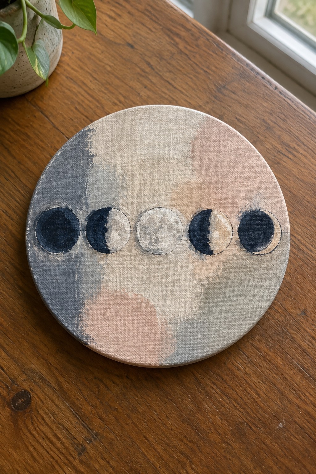 Row of moon phases on round canvas with abstract gray-pink background on wooden table