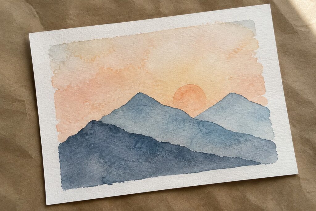 18 Easy Beginner Paintings Featuring Simple Mountain Scenes Watercolor painting of layered blue mountains under a soft orange sunset sky