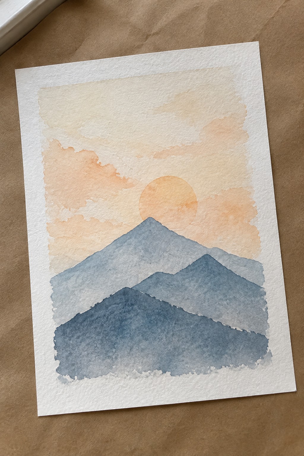 Watercolor painting of layered blue mountains under a soft orange sunset sky