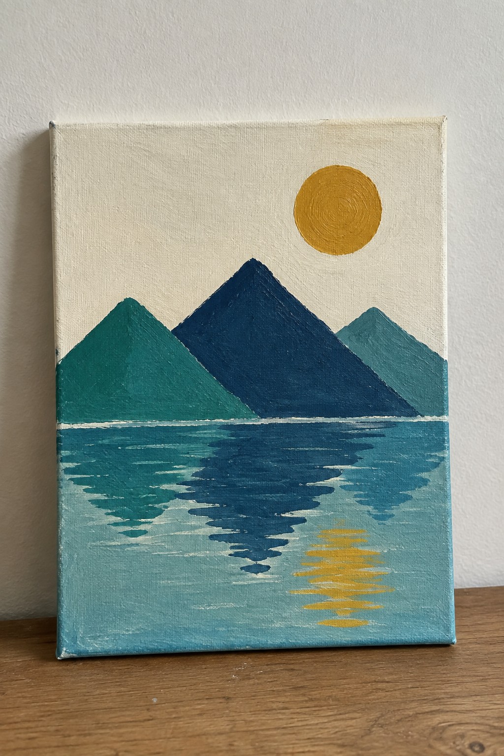 Minimalist painting of blue mountains reflected in turquoise water beneath yellow sun.