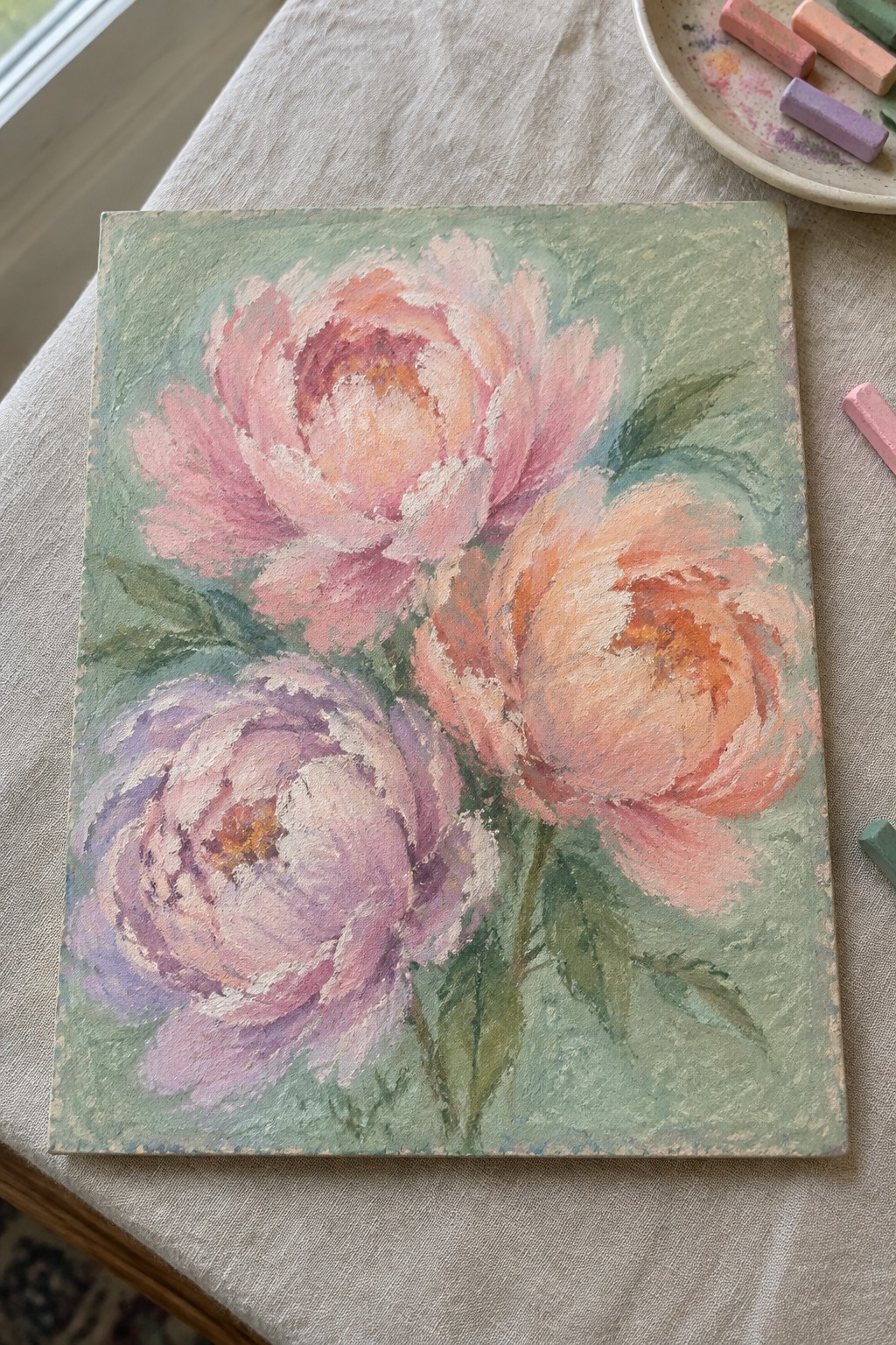 Pastel painting of three blooming peonies in pink, peach, and purple on green.