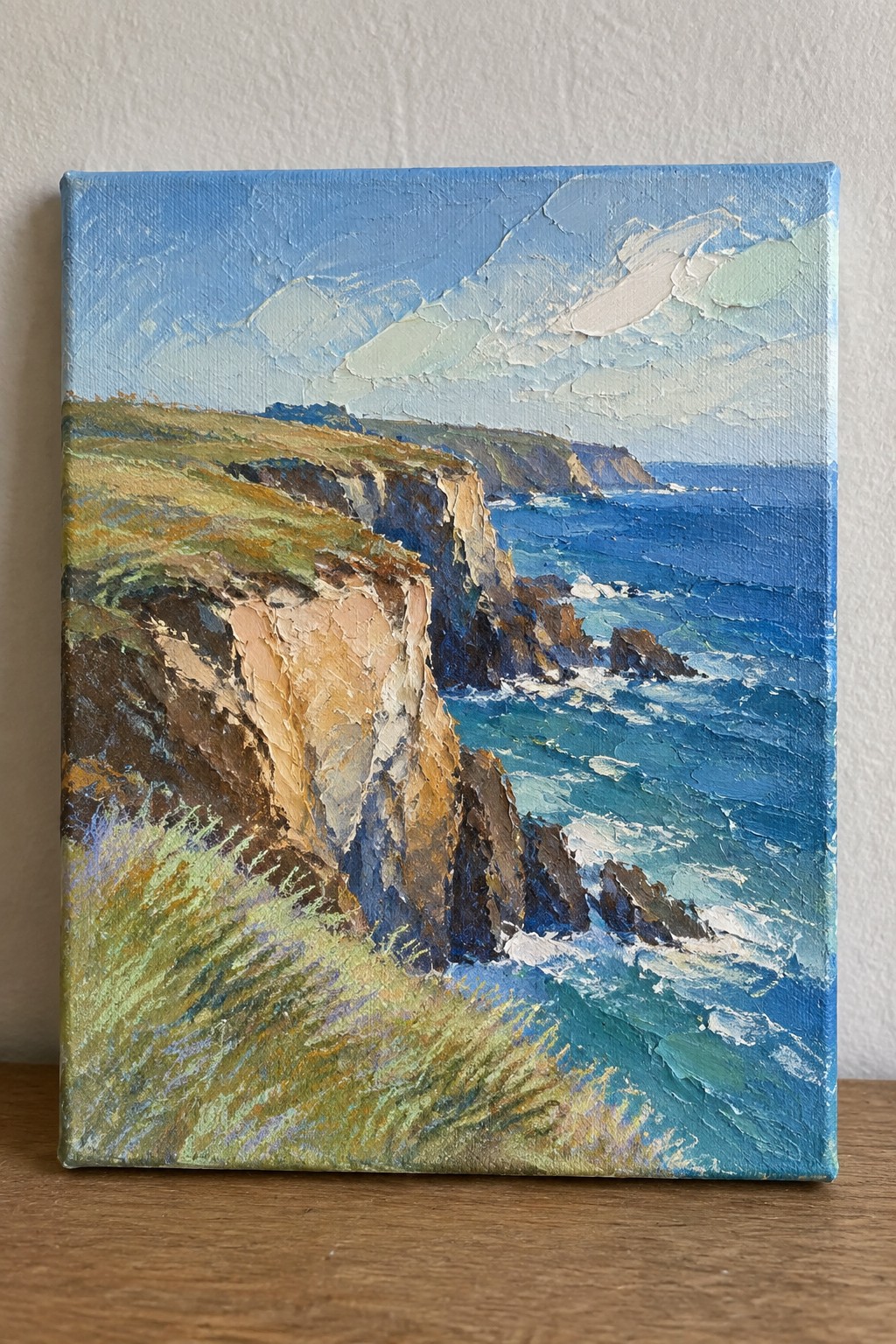Thickly textured oil painting of rugged cliffs by blue ocean waves under cloudy sky