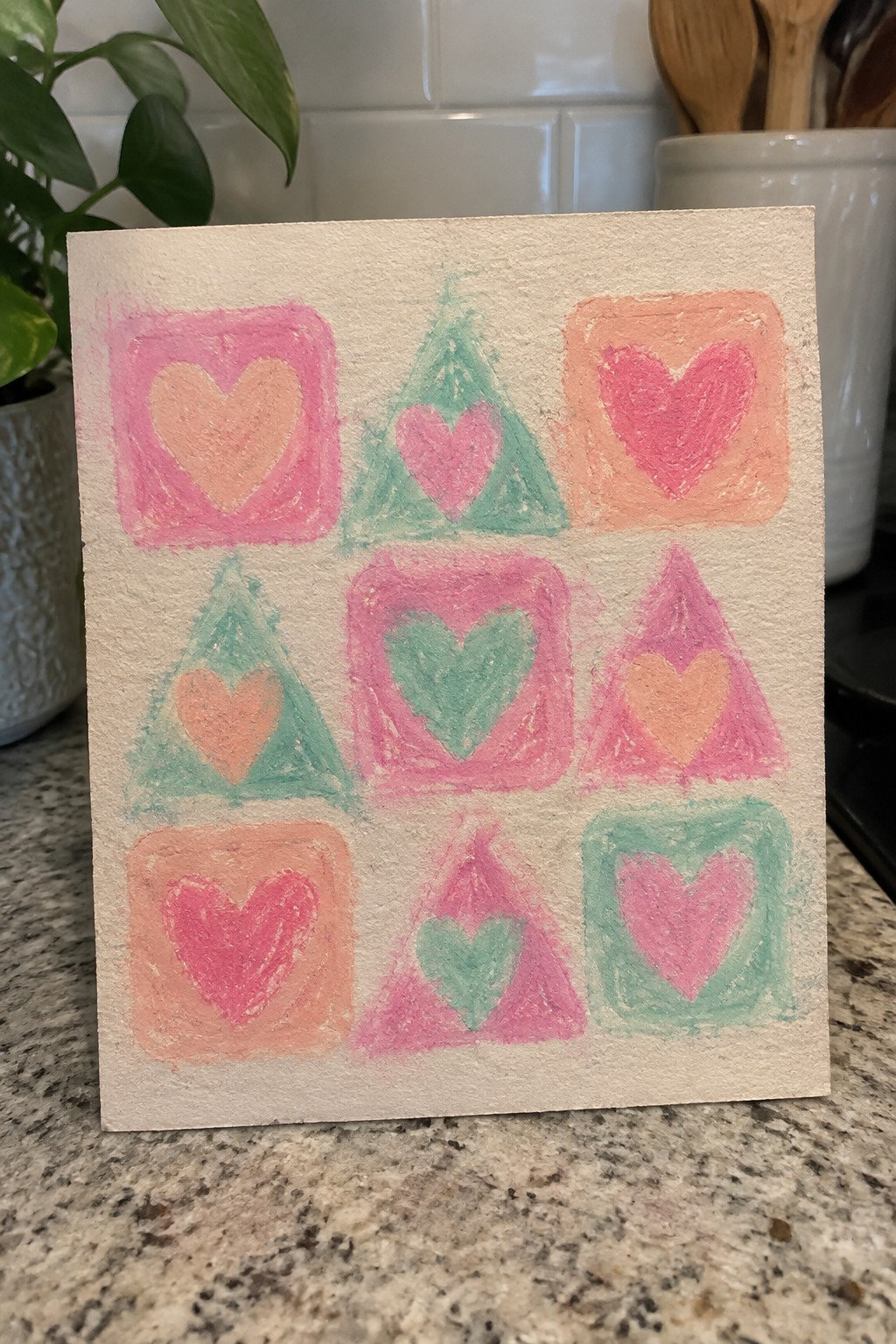 Colorful hearts painted inside pink squares, green triangles, and orange shapes on white paper.