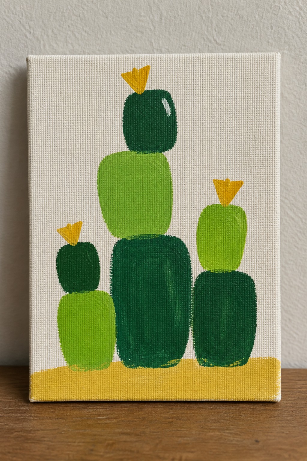 Abstract painting of three stacked green cacti with yellow tops on canvas