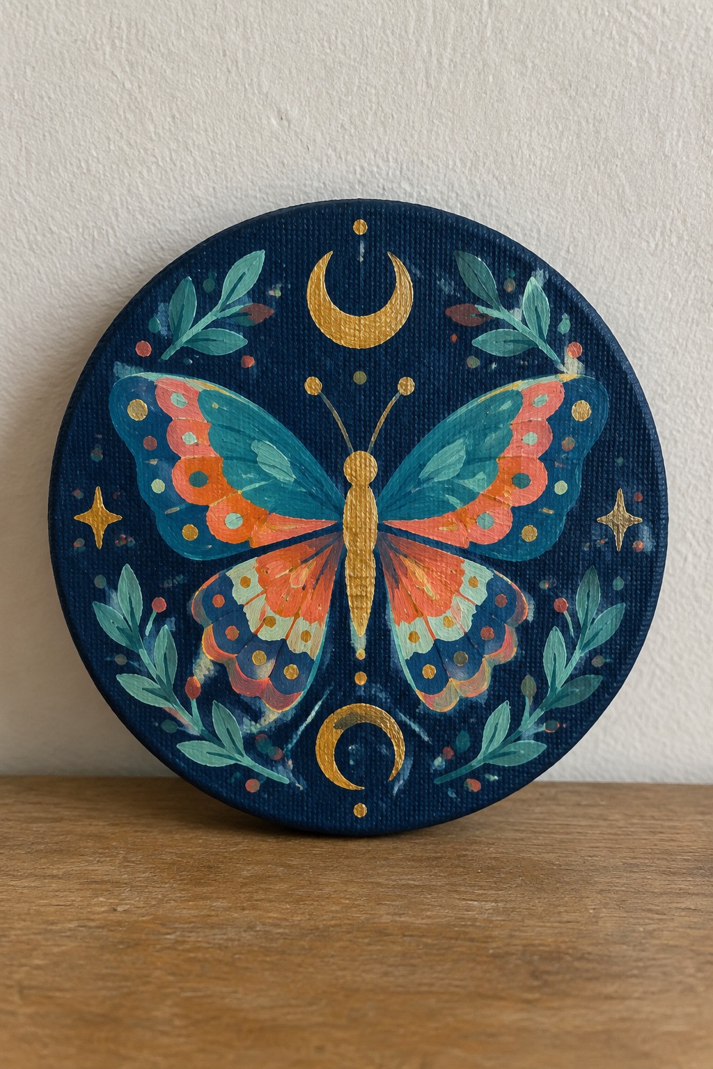 Round canvas painting of colorful butterfly with golden moons, stars and leaves on navy blue