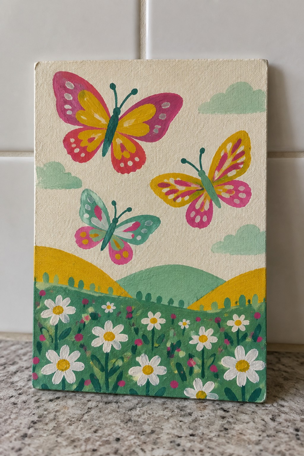 Three colorful butterflies flutter above daisies in a green meadow with hills.