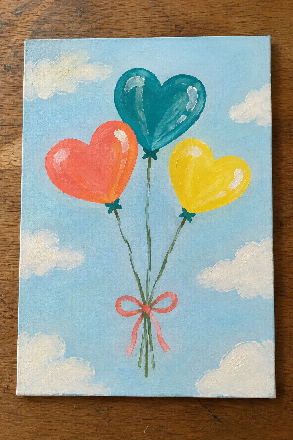 Three heart-shaped balloons in red, teal, and yellow tied with pink bow on blue sky.