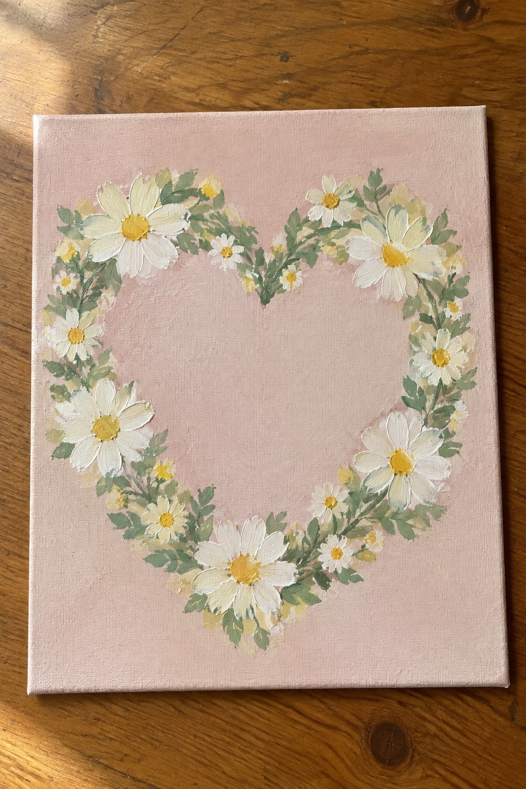 Heart-shaped wreath of white daisies with yellow centers on pink canvas
