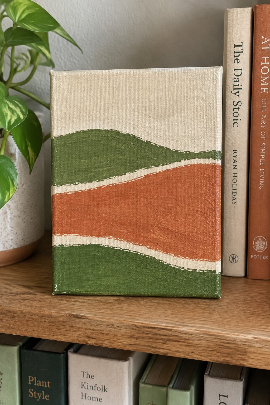 Abstract canvas with wavy green, orange, and beige stripes on wooden shelf beside books