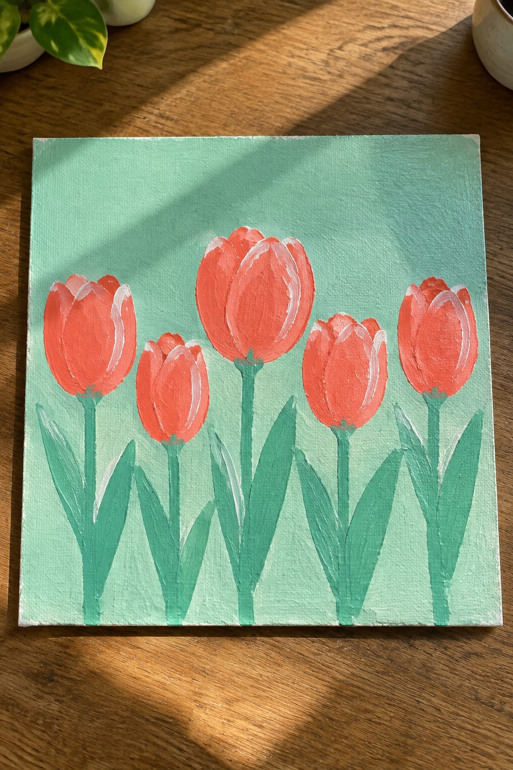 Five coral tulips with green stems on a mint green canvas