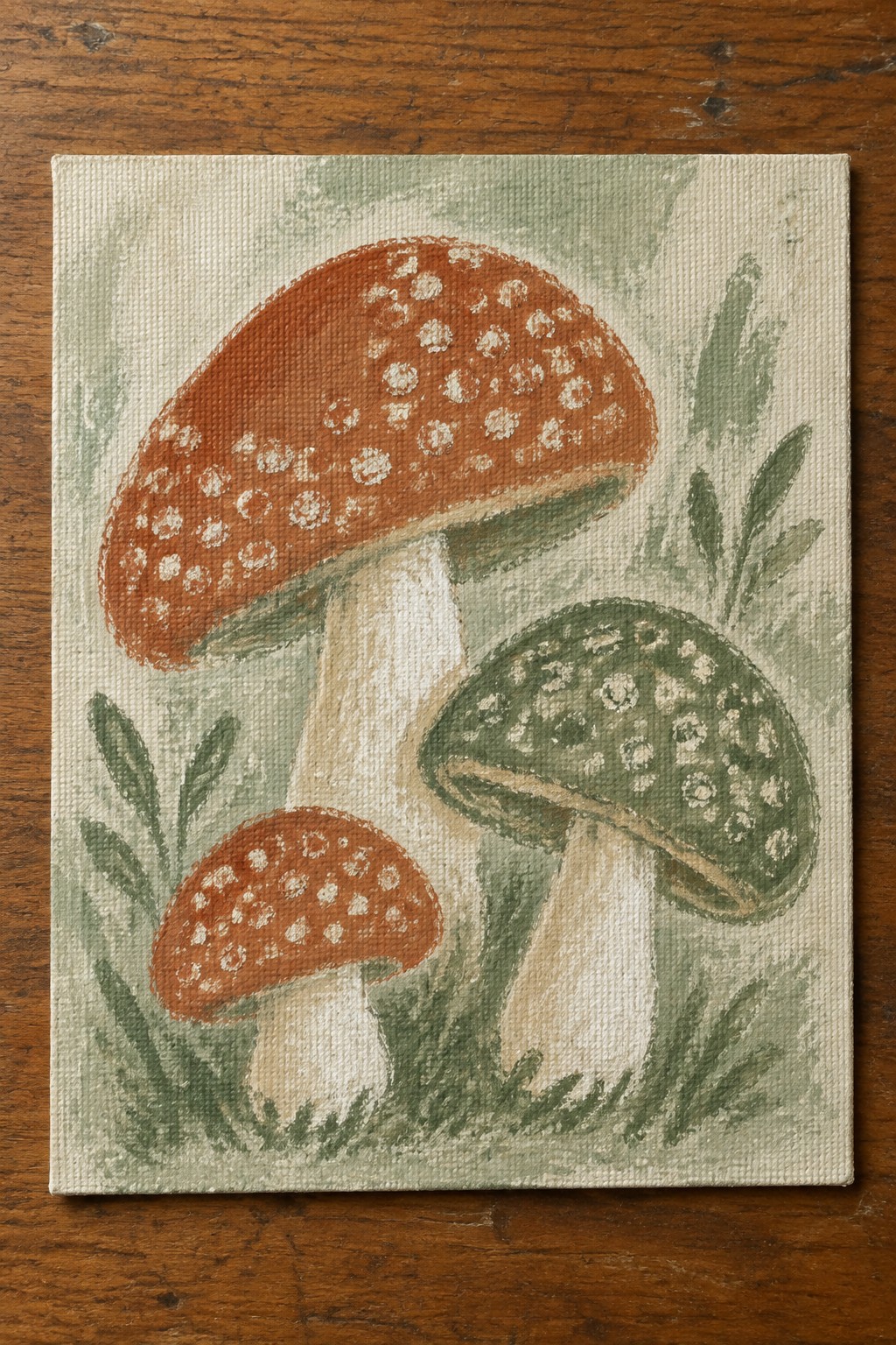 Three spotted mushrooms in red and green painted on canvas with foliage