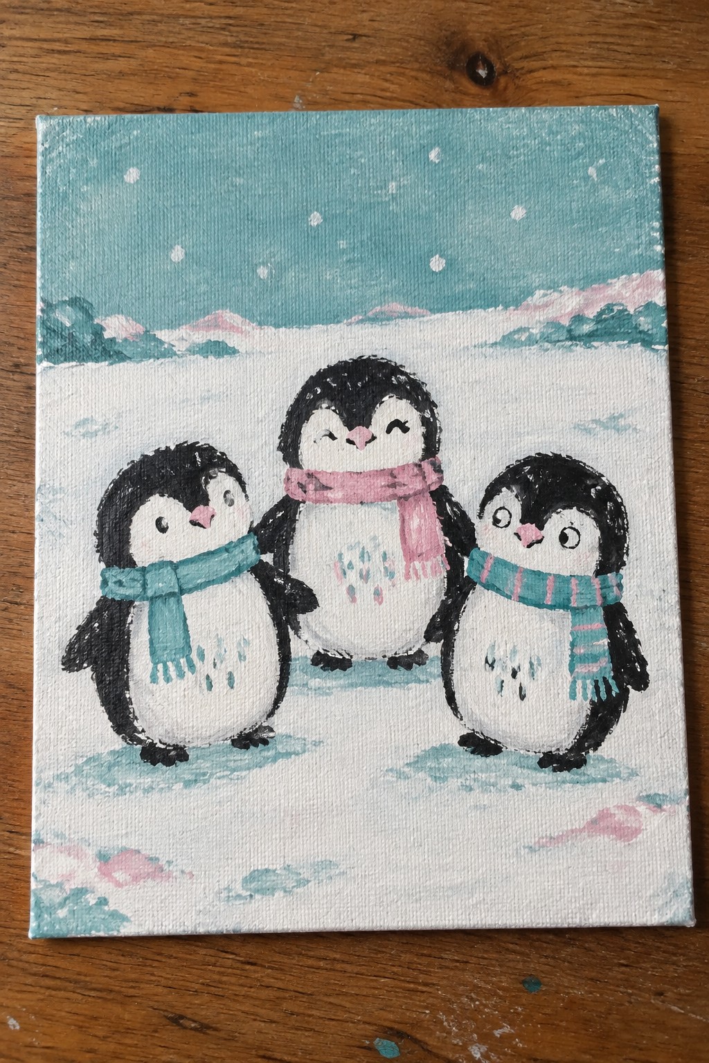 Three penguins in pink and teal scarves on a snowy mountain landscape painting