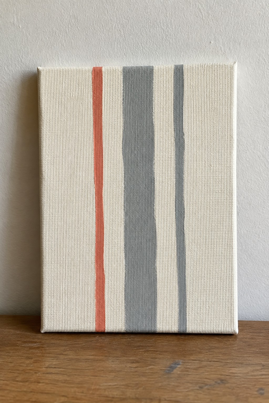 Canvas with vertical coral and gray stripes on wooden surface against white wall
