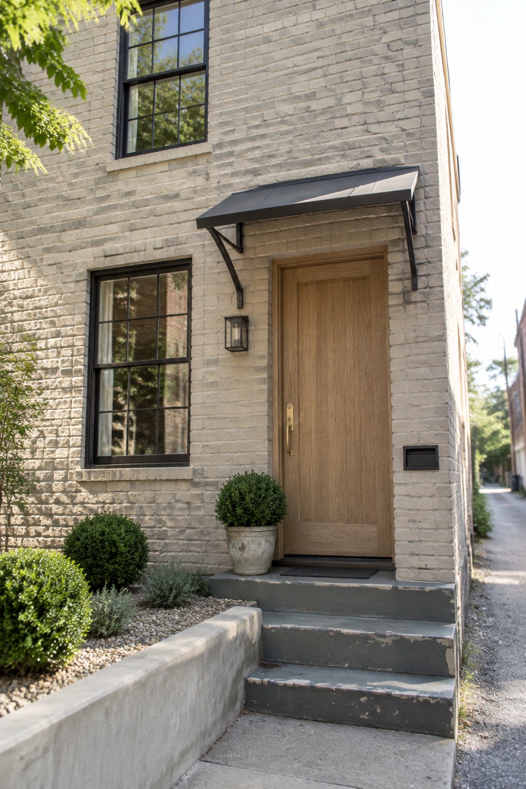 Light brick building entrance with wooden door, black awning, gray steps, and potted plants