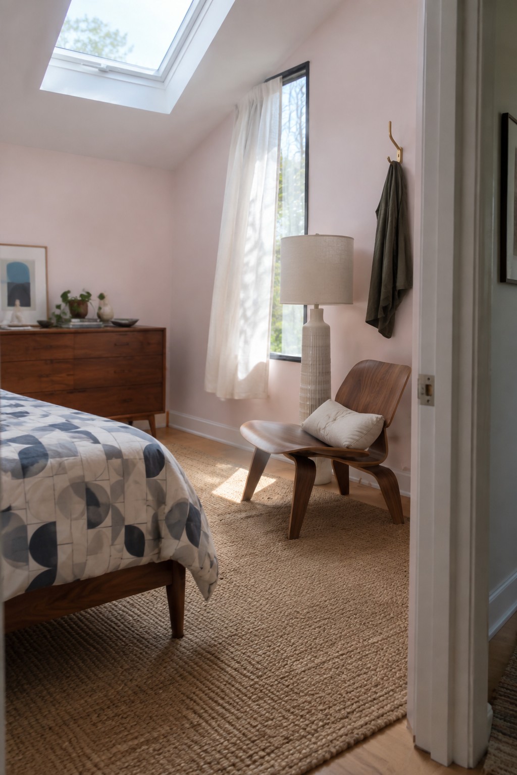 Cozy pink bedroom with wooden bed, lounge chair, woven rug, and skylight.