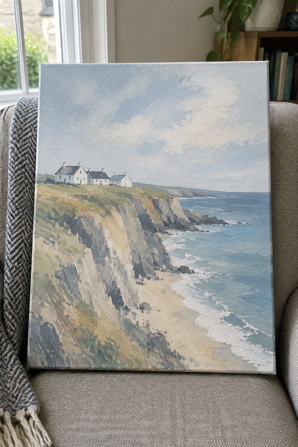 Painting of white houses on sea cliffs with beach below, resting on gray couch.