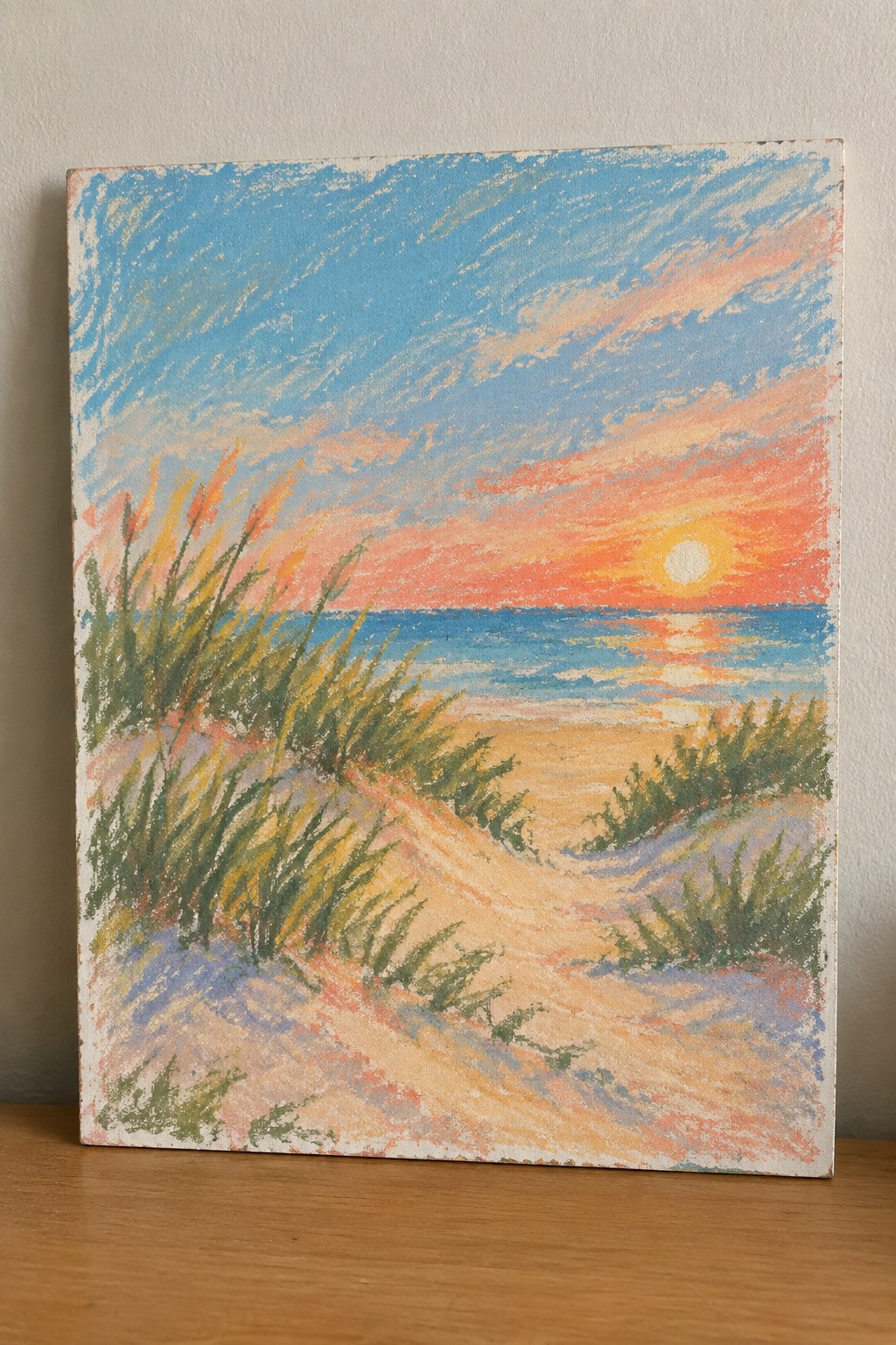 Pastel beach sunset with grassy sand dunes, blue ocean, and orange sky.
