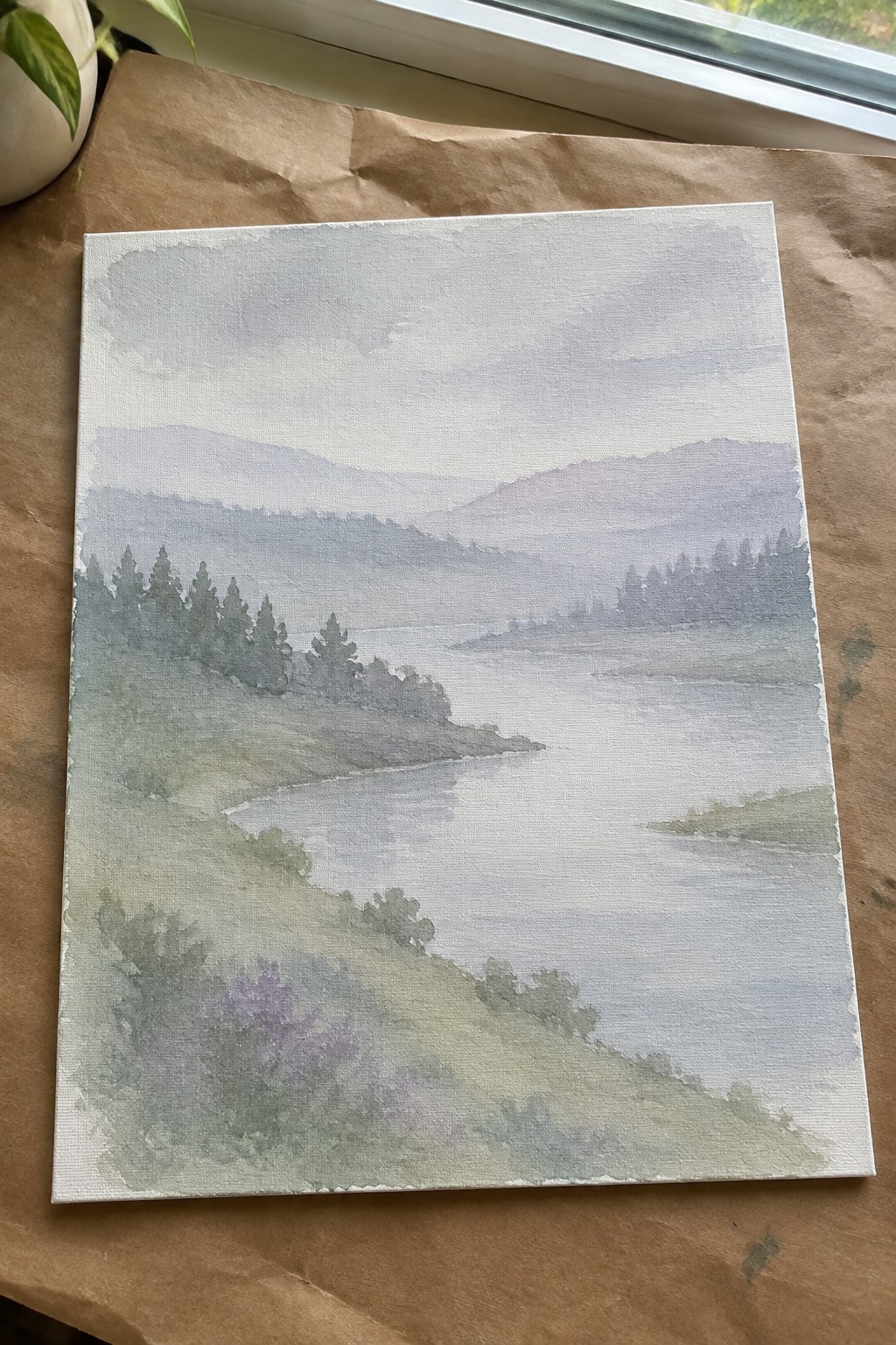 A watercolor landscape painting on canvas showing a misty river winding through green and purple hills with scattered trees.