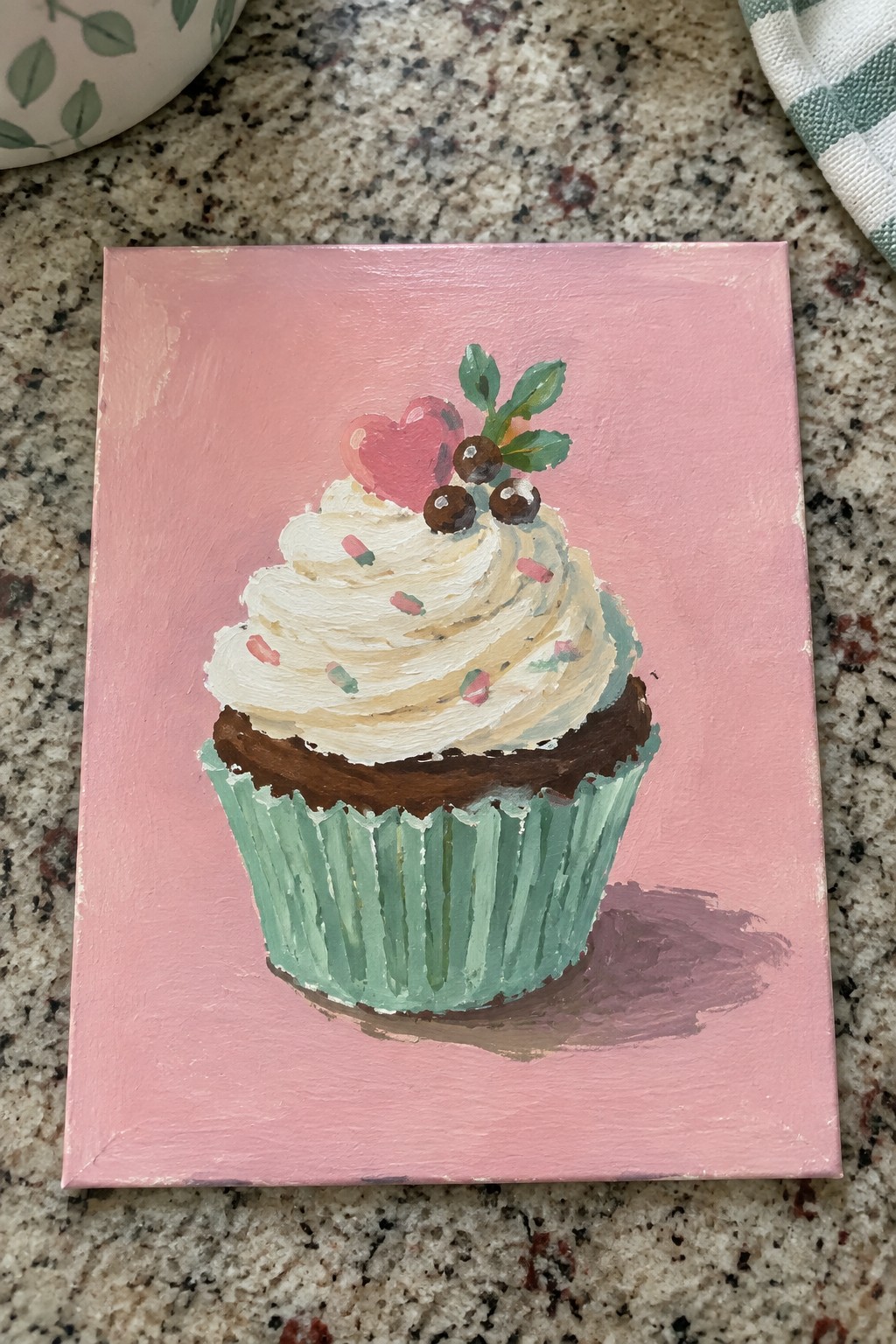 Acrylic painting of chocolate cupcake with white frosting and pink heart on pink canvas