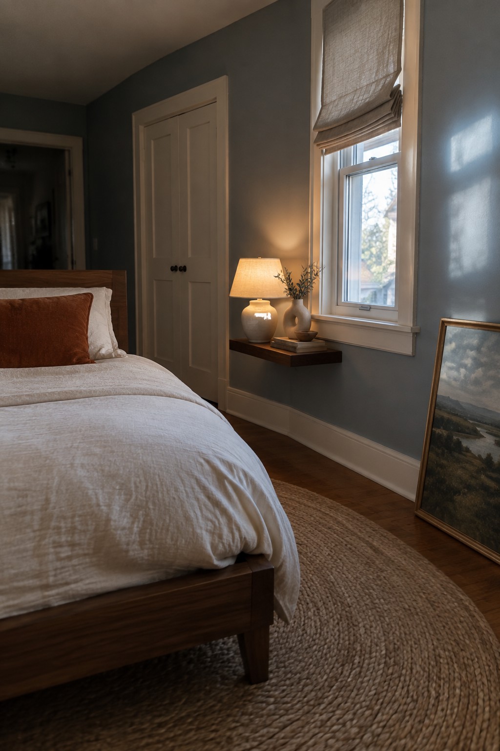 Cozy bedroom with wooden bed, white linens, floating shelf lamp, and woven rug.