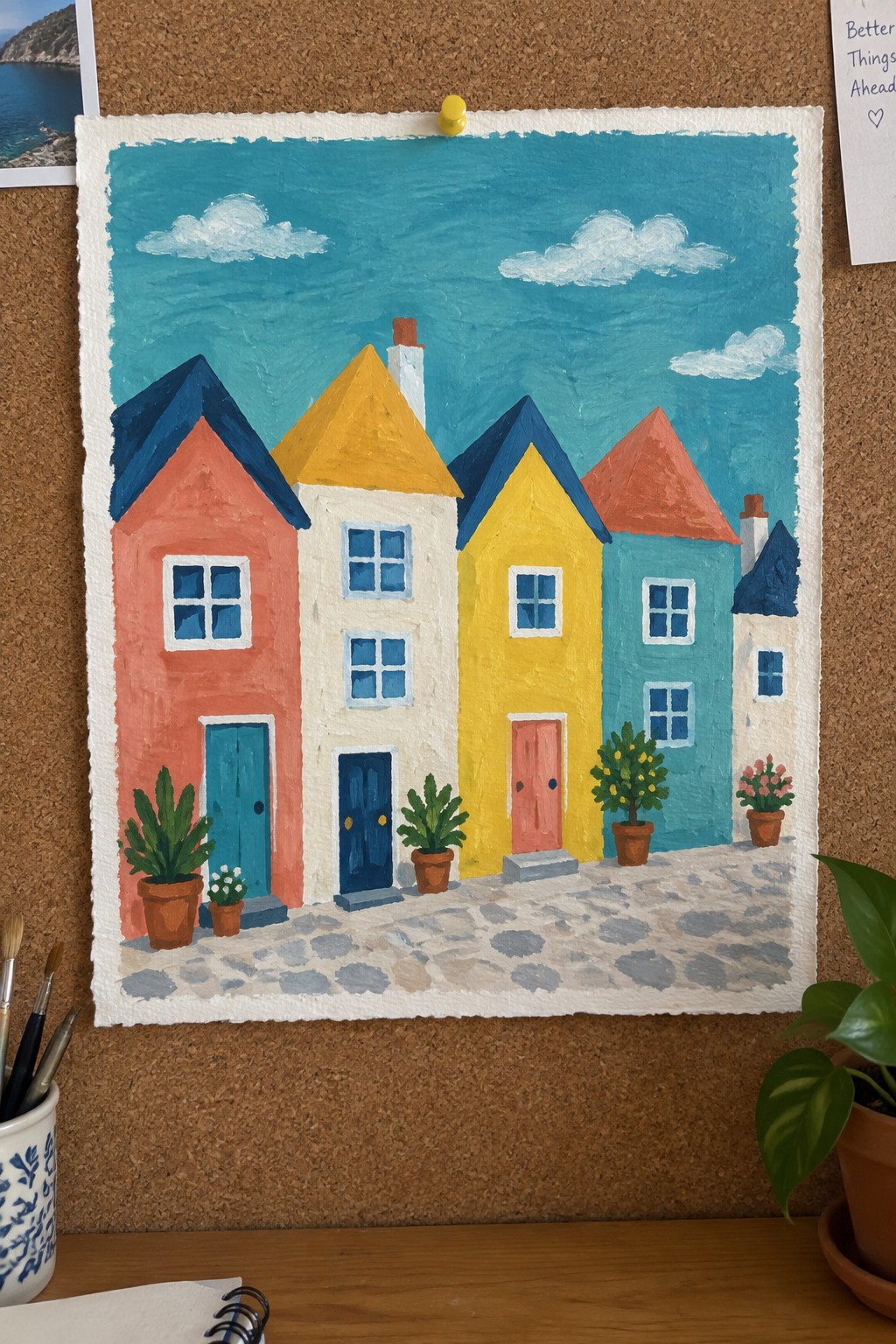 Vivid painting of colorful houses with peaked roofs along a cobblestone street and potted plants.