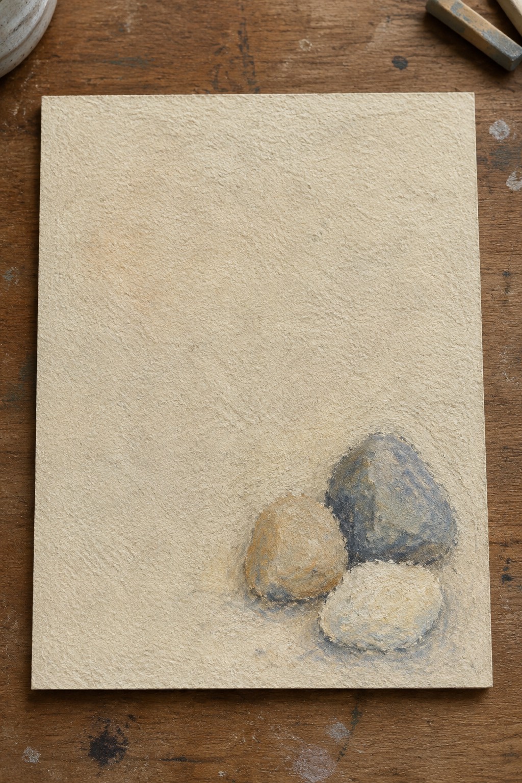 Three rounded stones in soft pastels on textured beige paper over wood