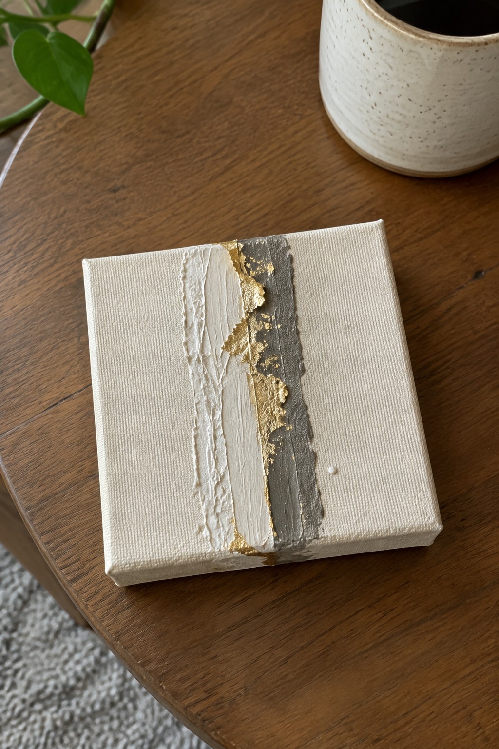Small canvas with white texture, gold leaf, and gray vertical stripe on wooden table