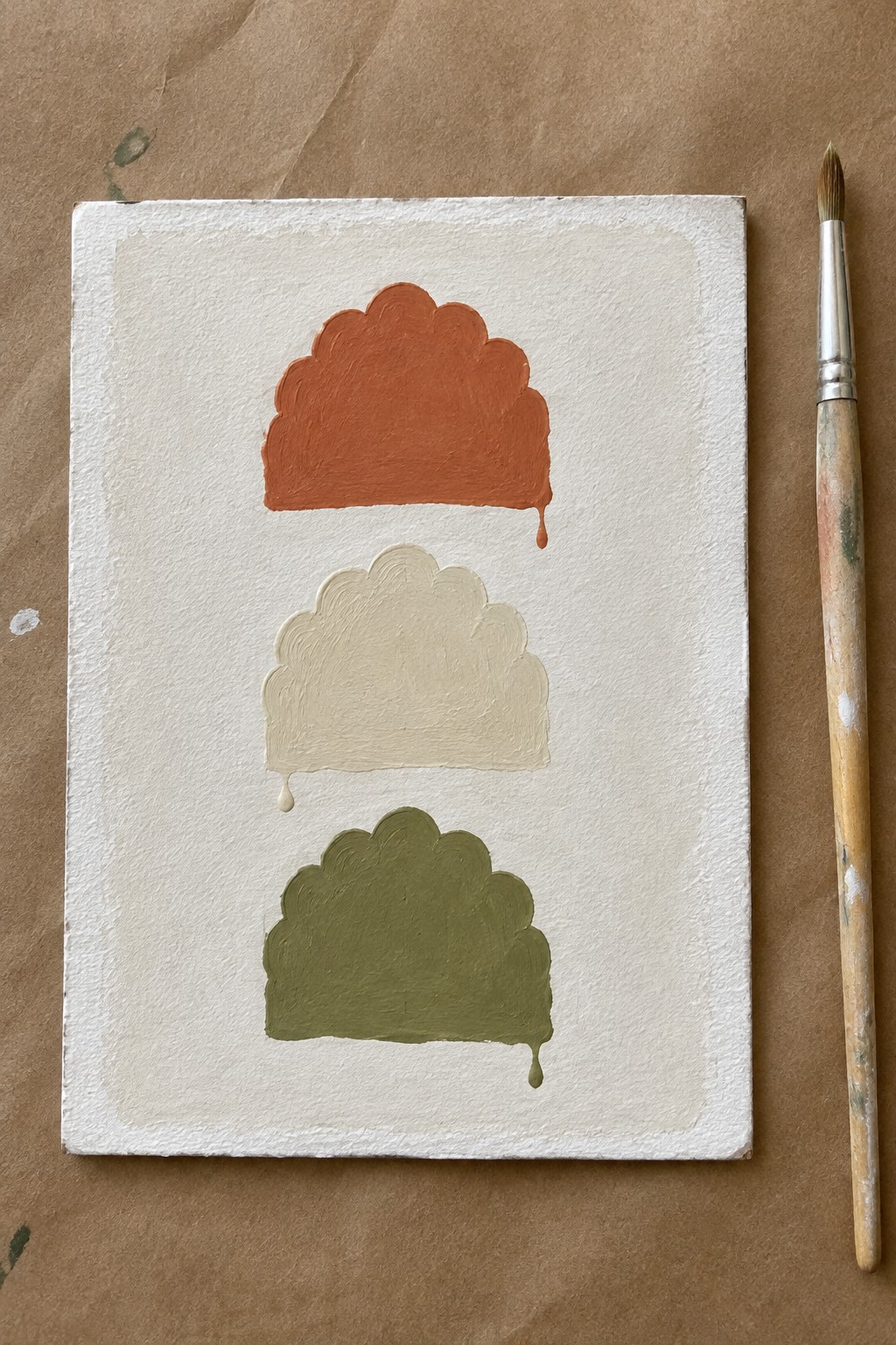 Three scalloped shapes in orange, beige, and green with drips beside a brush