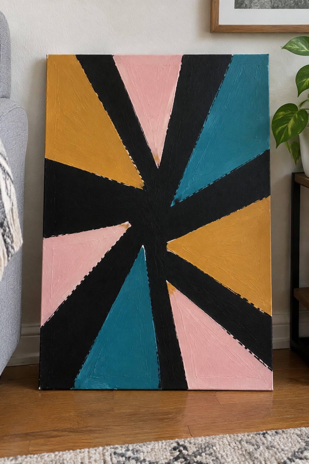 Abstract painting with radiating triangles in yellow, pink, teal, and black on wooden floor.