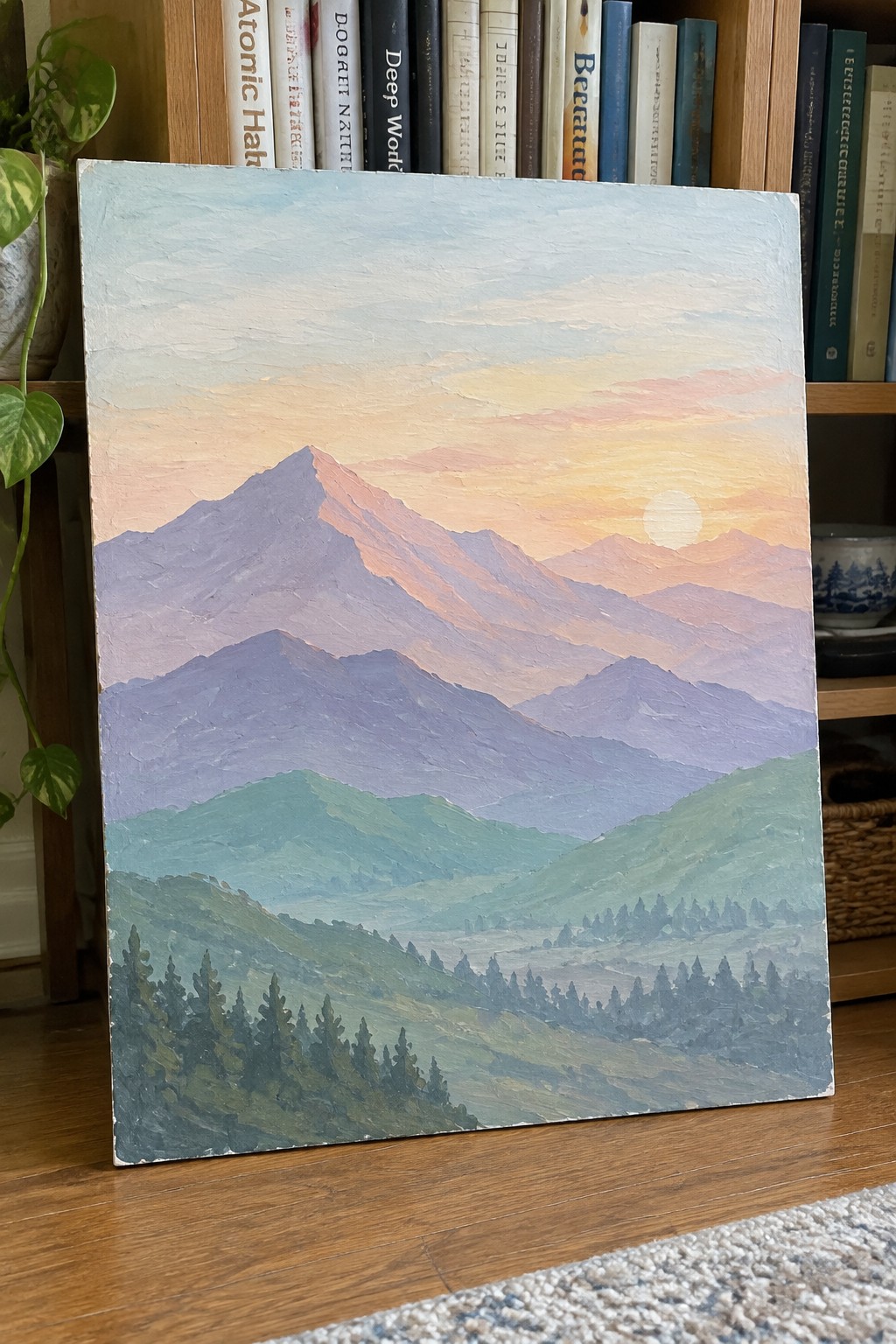 Layered purple mountains at sunset painting leaning against bookshelf with books