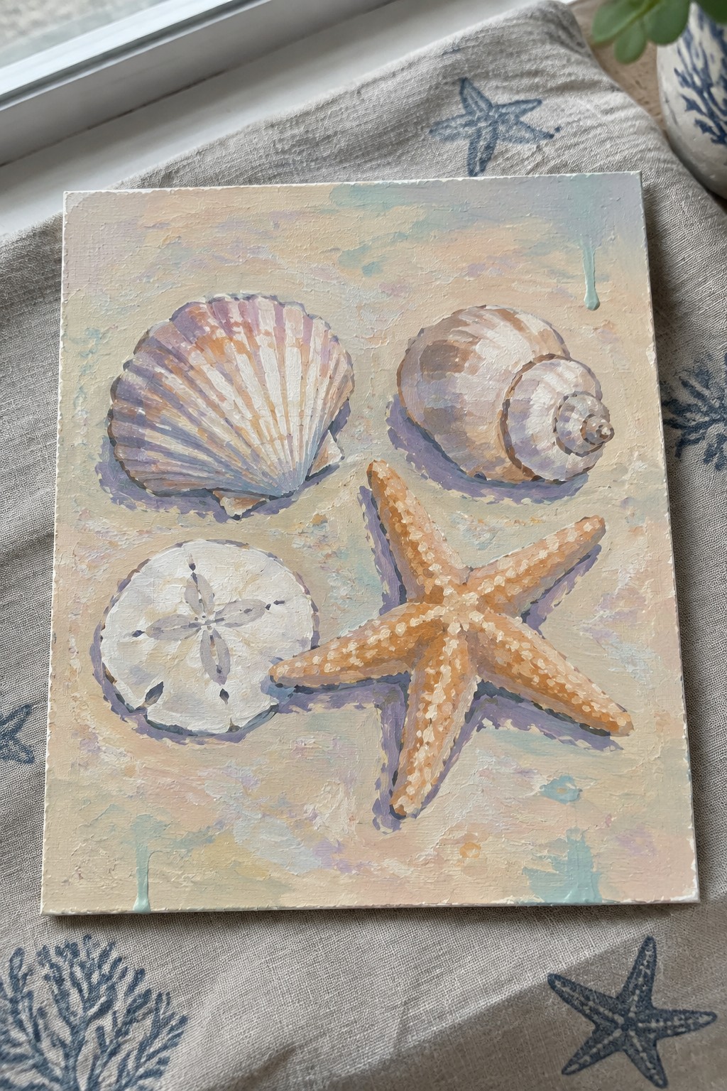 Painting of seashells, sand dollar, and orange starfish on sandy pastel background