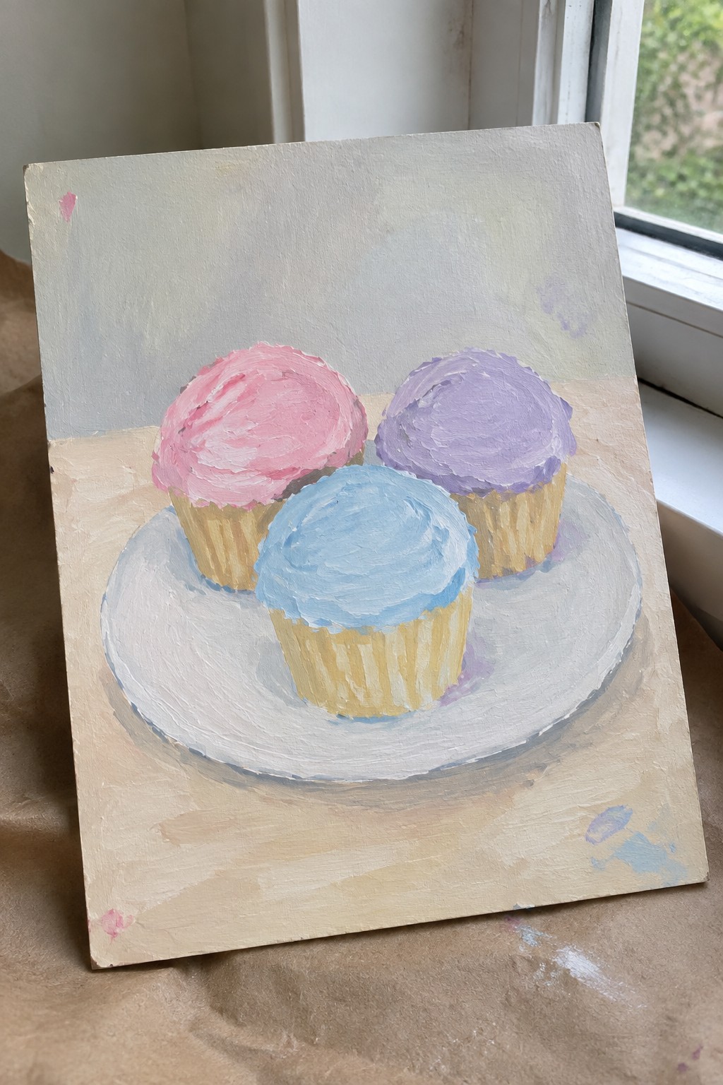 Three cupcakes with pink, blue, and purple frosting on a white plate.