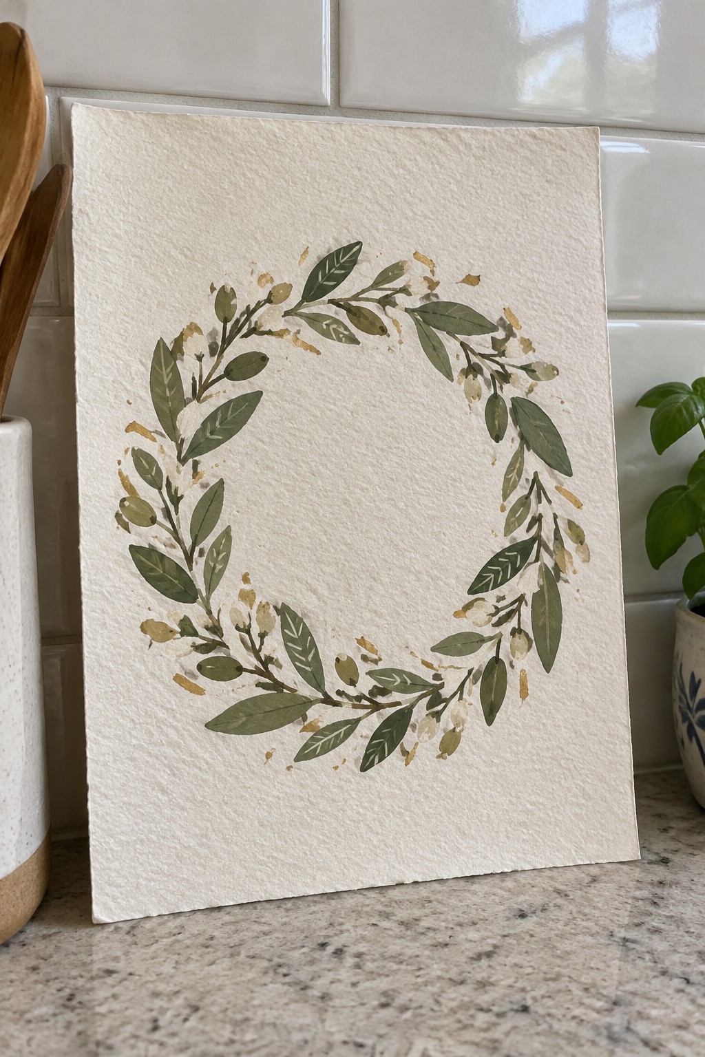 Watercolor wreath of green leaves with gold accents on textured paper