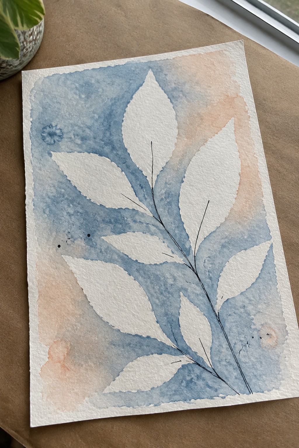 A watercolor painting showing white leaf shapes against a blue and peach wash with black ink stems and one small blue flower.