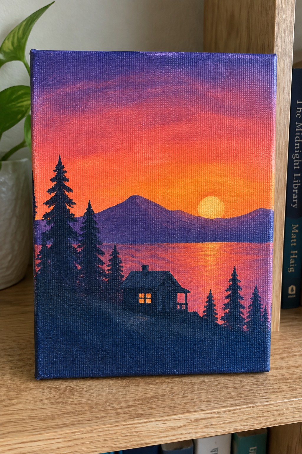 Vibrant sunset painting with orange-red sky, purple mountains, silhouetted cabin and pine trees