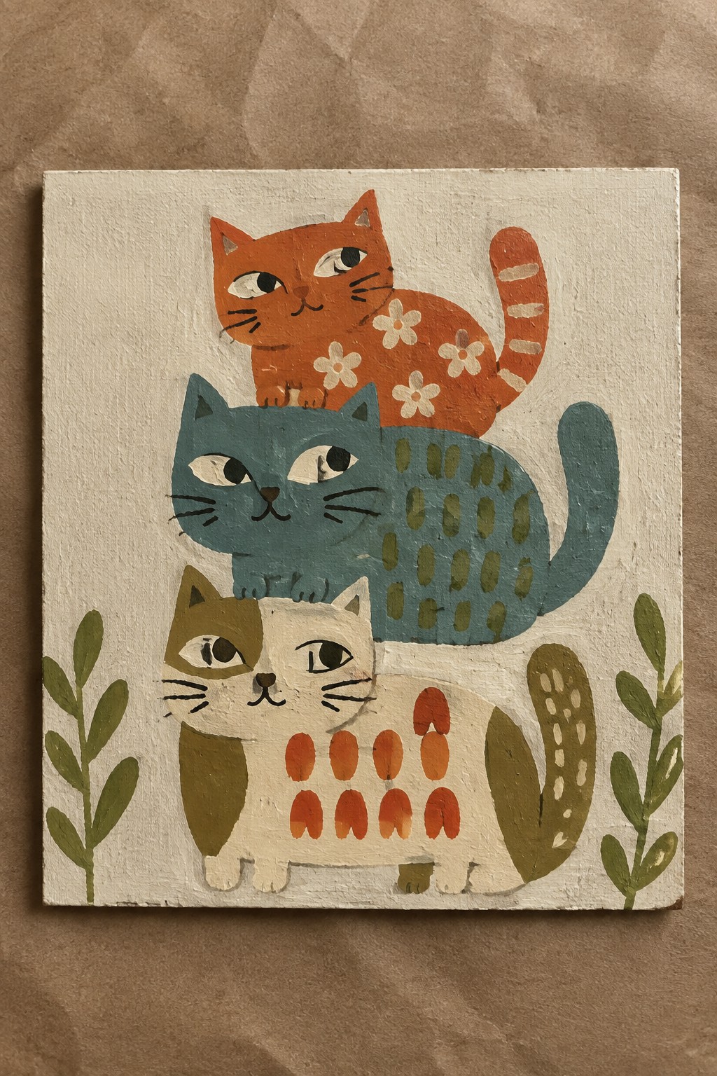 Three stylized cats stacked vertically on a small canvas, with an orange cat on top, a teal cat in the middle, and a white and brown cat at the bottom, plus green plant shapes on the sides.