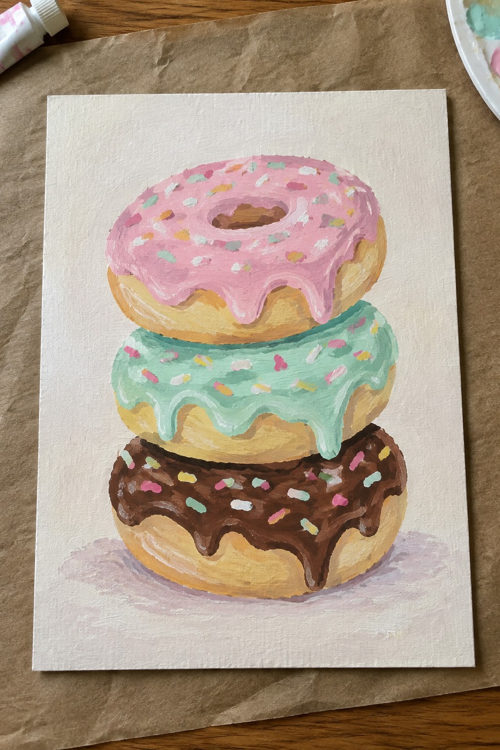 Three stacked donuts with pink, mint green, and chocolate icing plus sprinkles on canvas