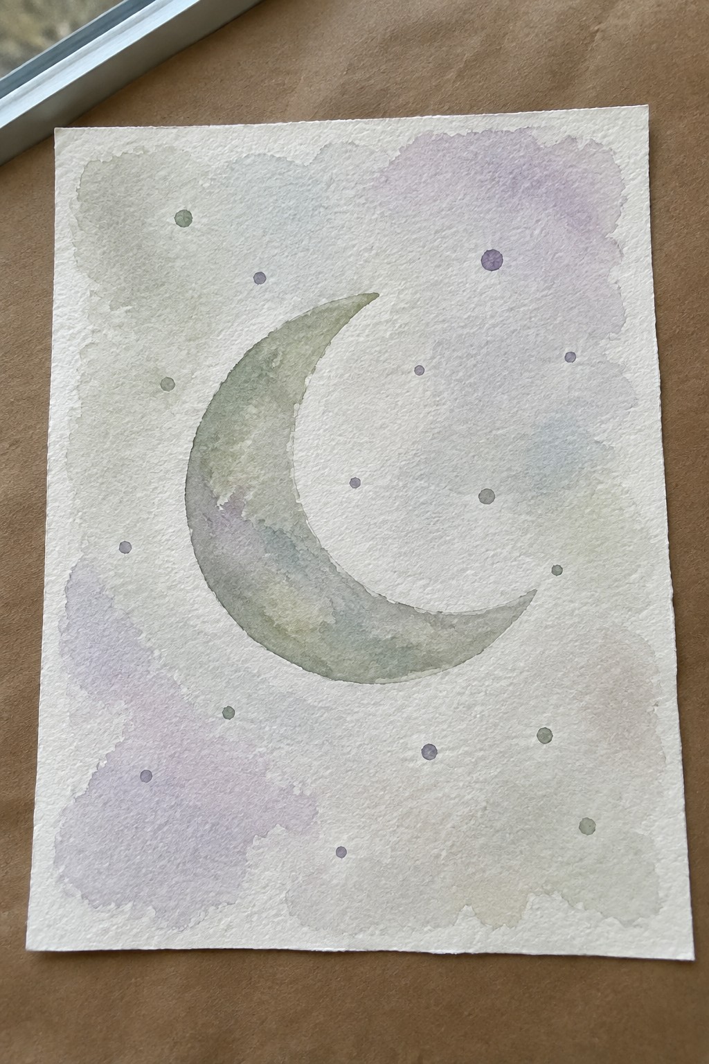 Crescent moon in soft watercolor greens and purples with scattered stars on paper