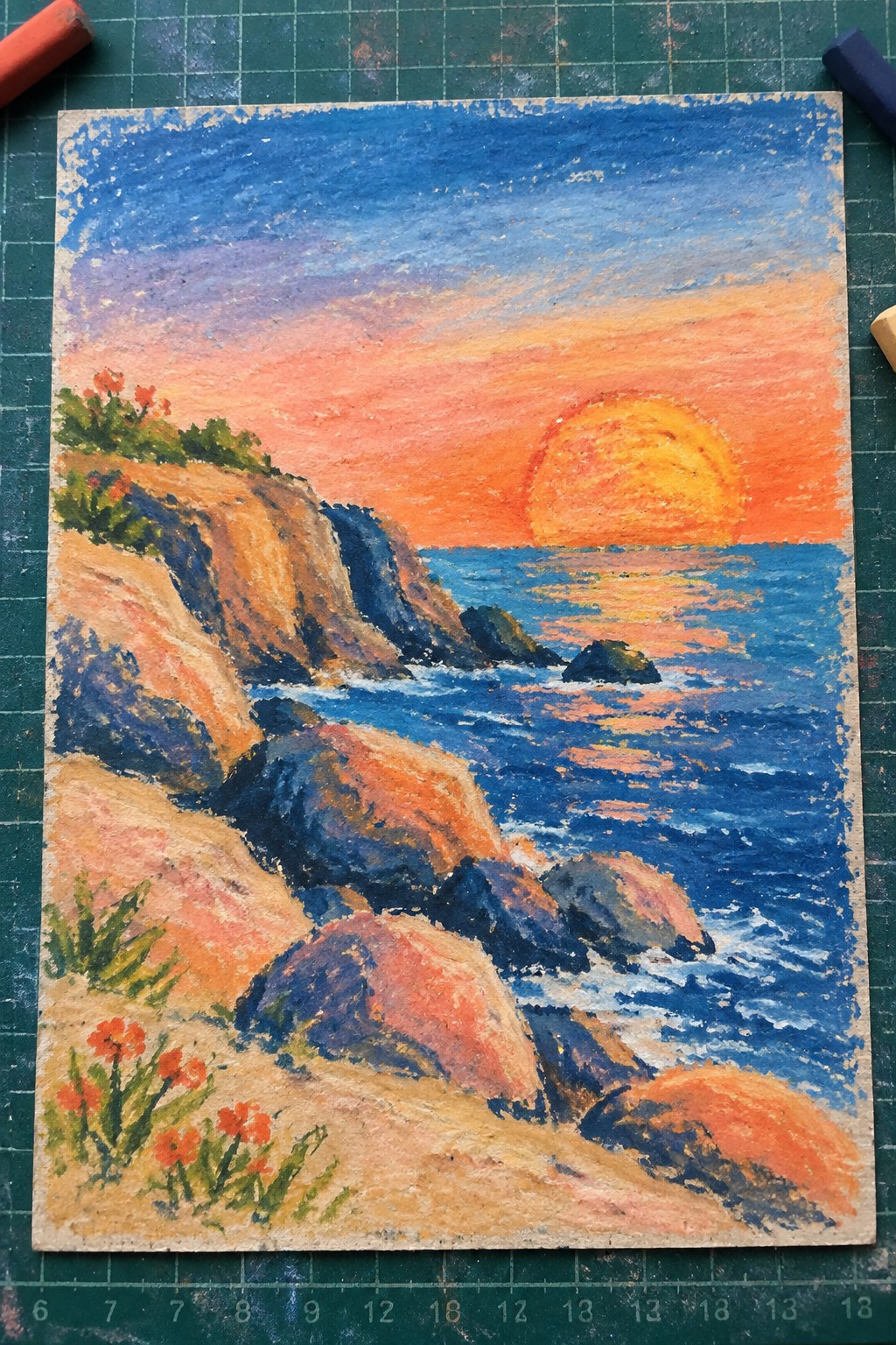 Pastel seascape of vibrant sunset over blue ocean with rocky cliffs and red flowers.