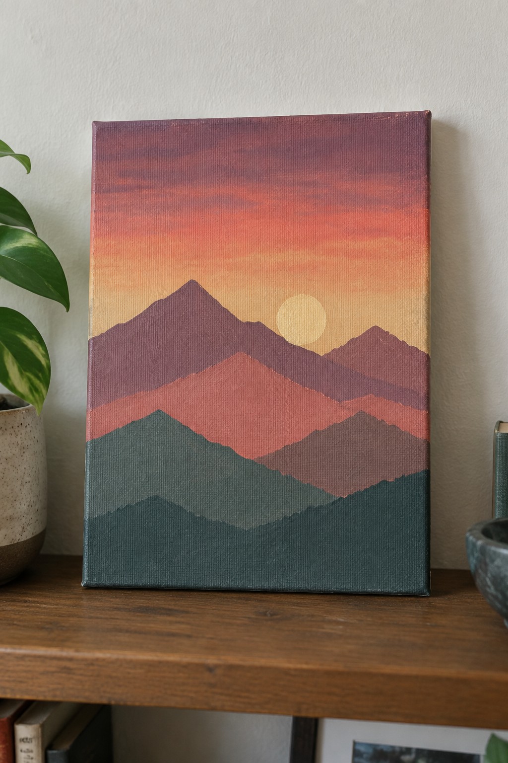 Layered mountain painting in sunset colors on wooden shelf beside plant